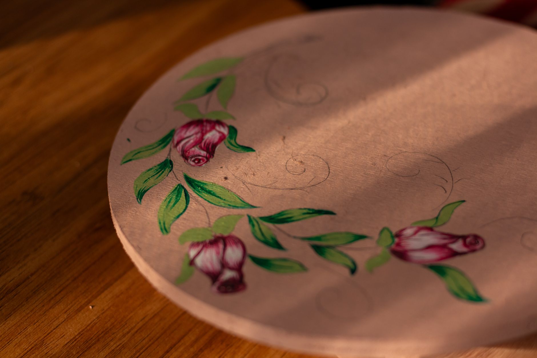 Close-up of a hand-painted floral design on a circular canvas with roses and leaves.