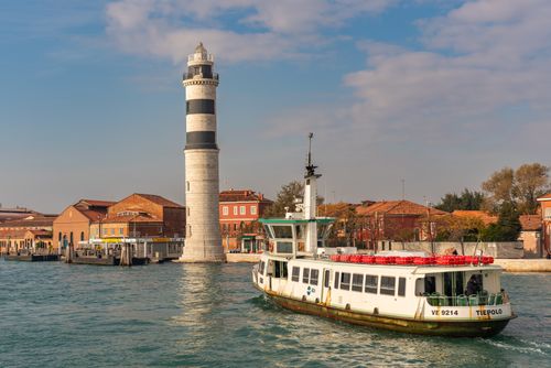 Free Sunny day at Murano Island, showcasing the iconic lighthouse and a ferry in Venice, Italy. Stock Photo