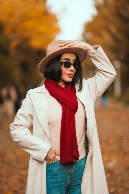 Stylish woman in autumn fashion with red scarf and beige hat outdoors.