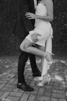 Elegant black and white photo of newlyweds embracing, highlighting tattoo and footwear.