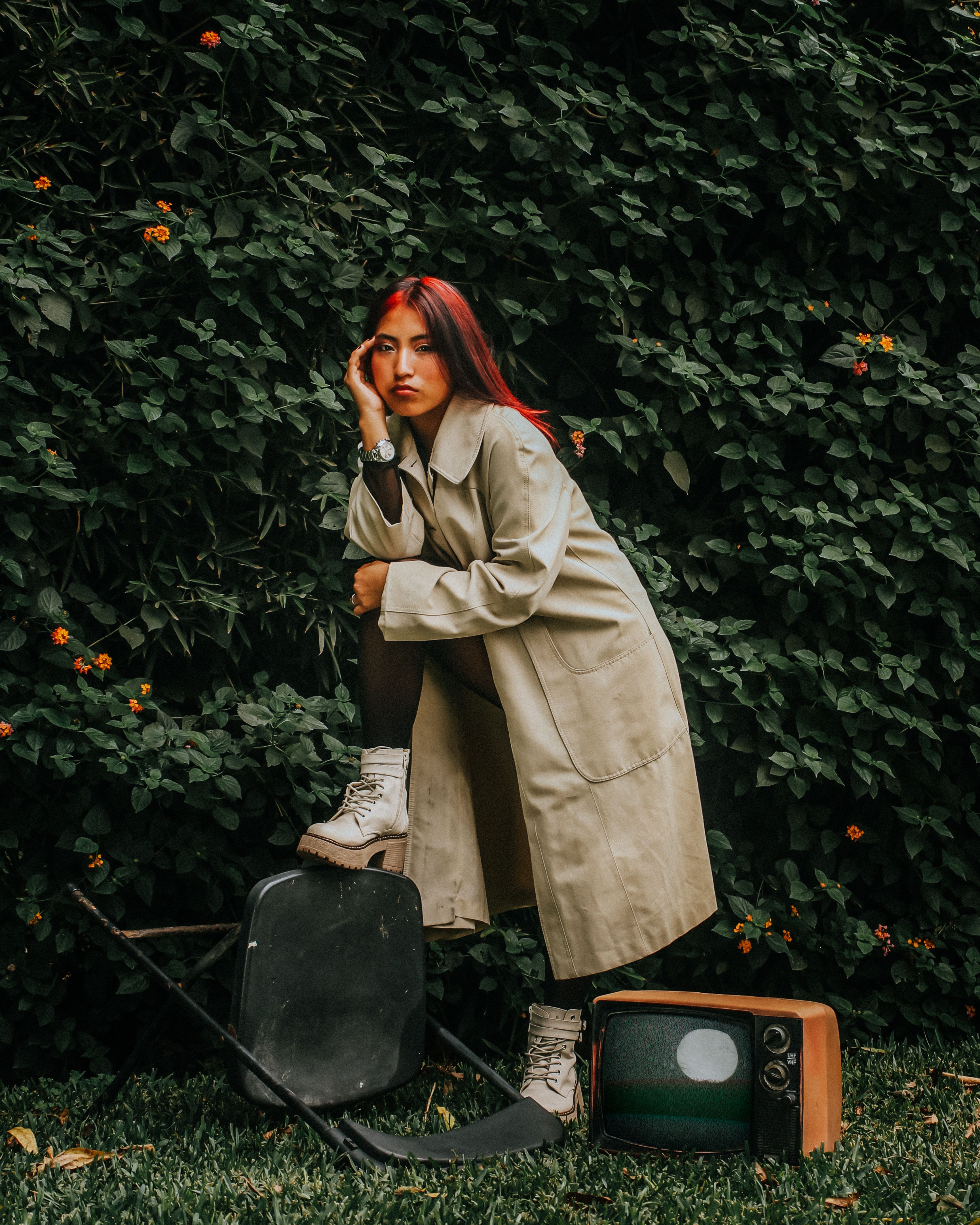 Fotomural Una mujer posa junto a un televisor antiguo con un exuberante jardín como telón de fondo, transmitiendo un aire retro.