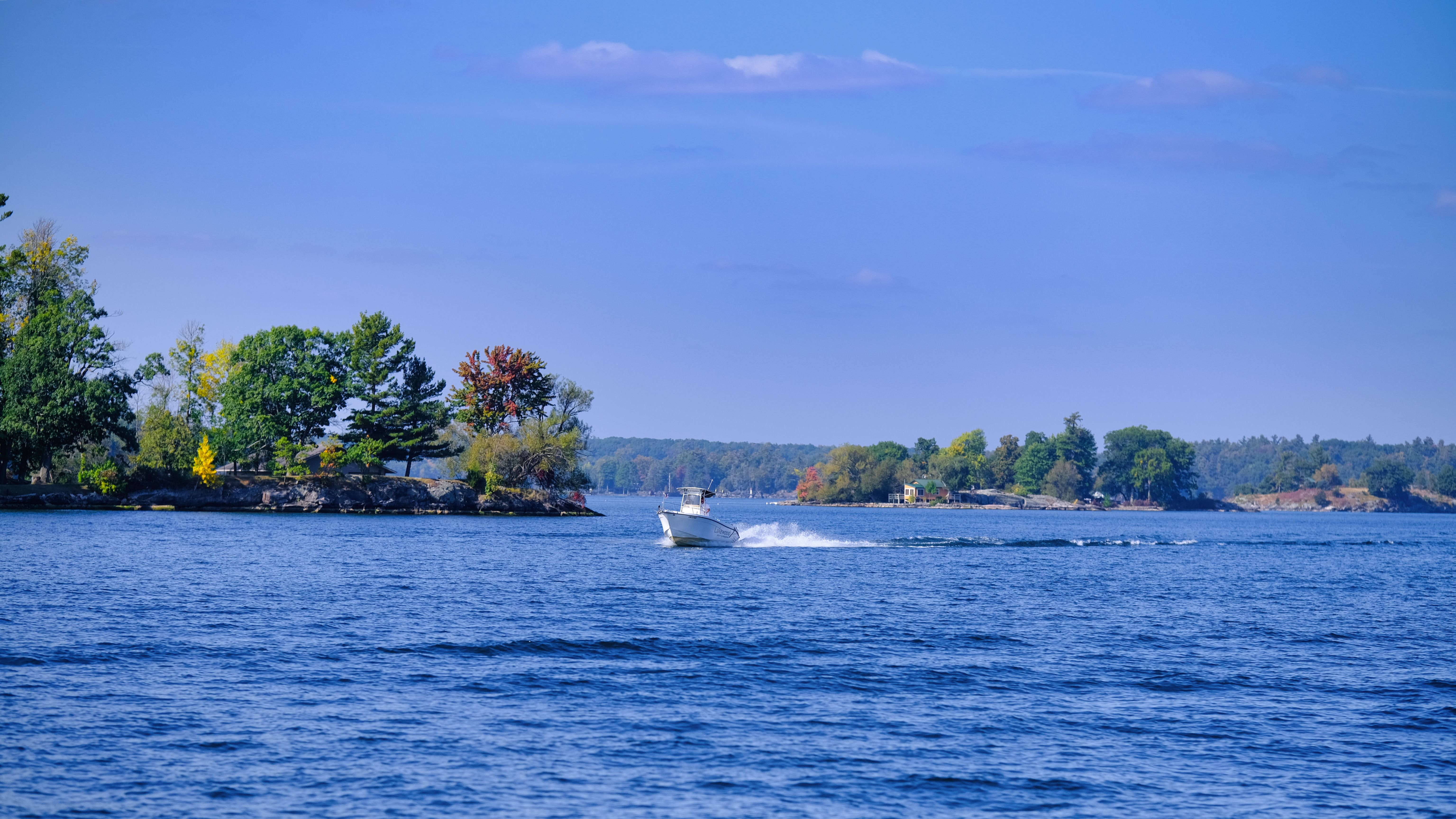 A serene lake with a boat cruising past vibrant autumn foliage under a clear blue sky.