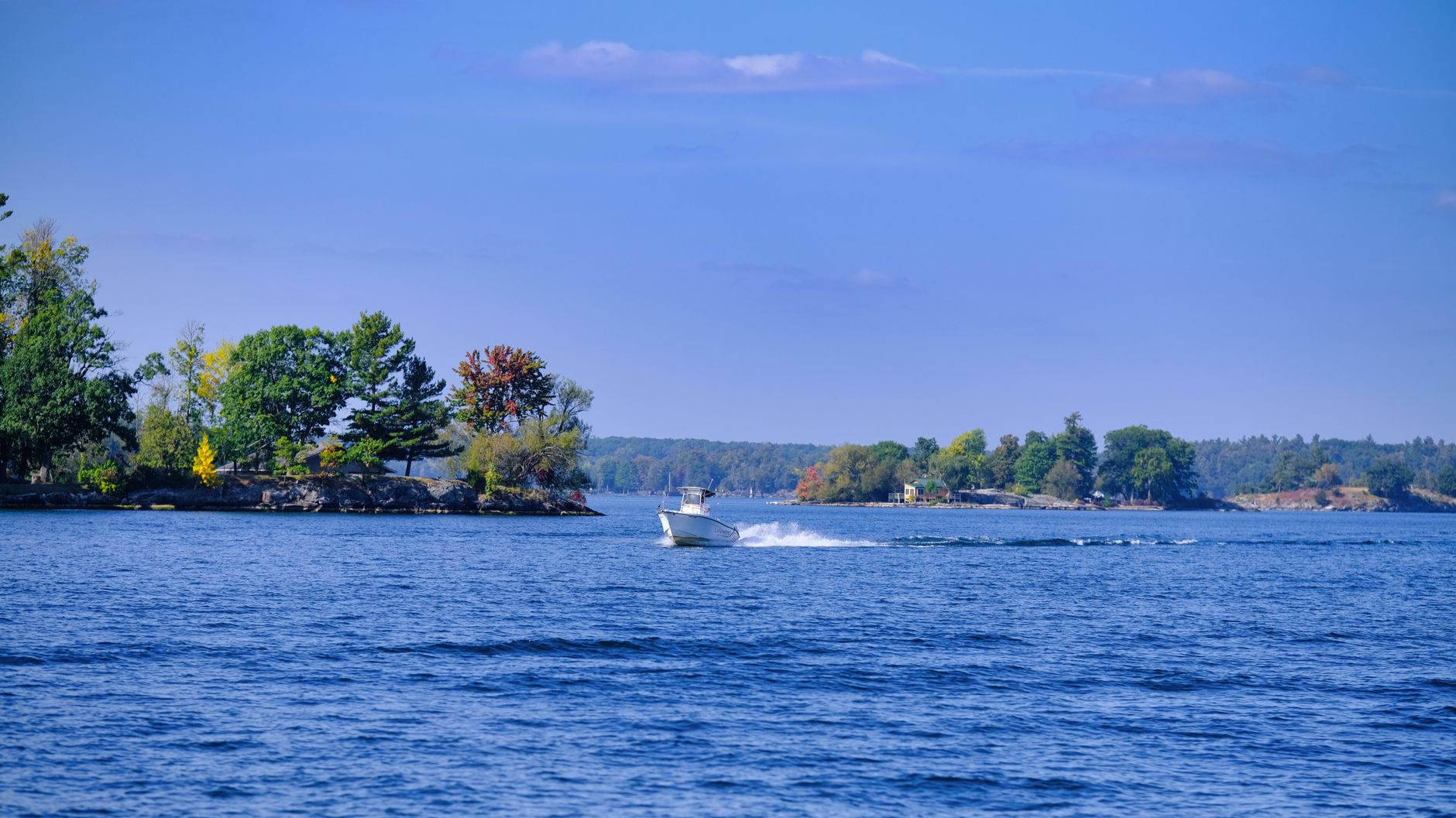 A serene lake with a boat cruising past vibrant autumn foliage under a clear blue sky.