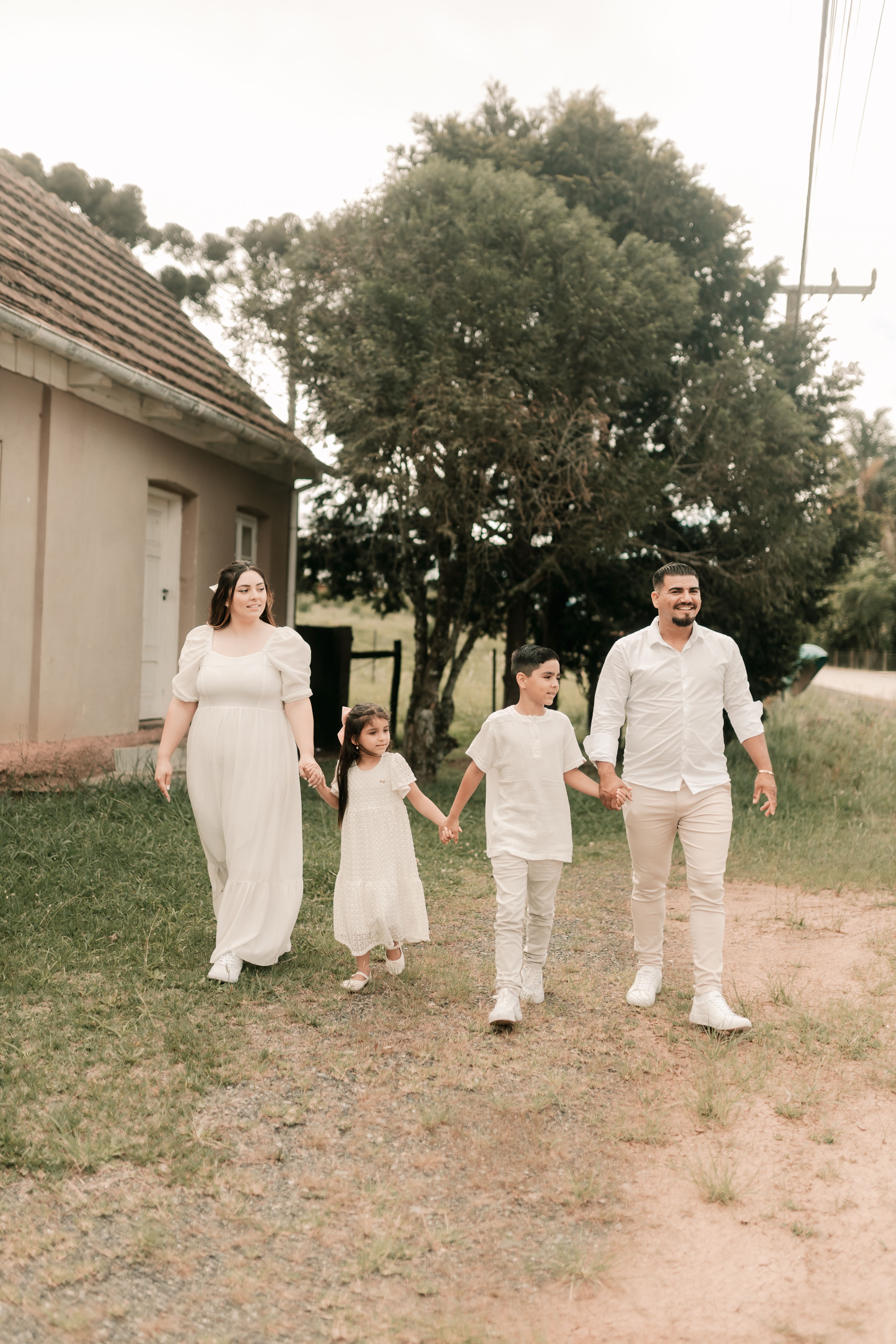 A joyful family walking hand in hand outdoors in casual white clothing.