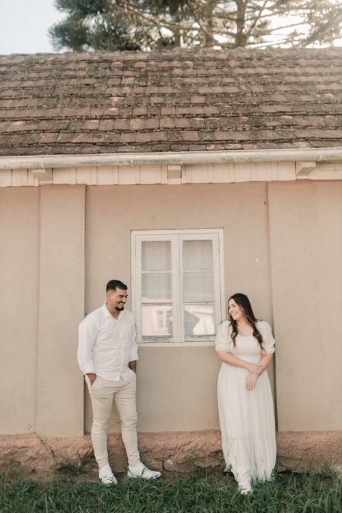 Free A couple stands smiling in front of a rustic house, exuding warmth. Stock Photo