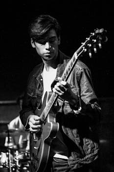Black and white photo of a young man intensely playing an electric guitar on stage.