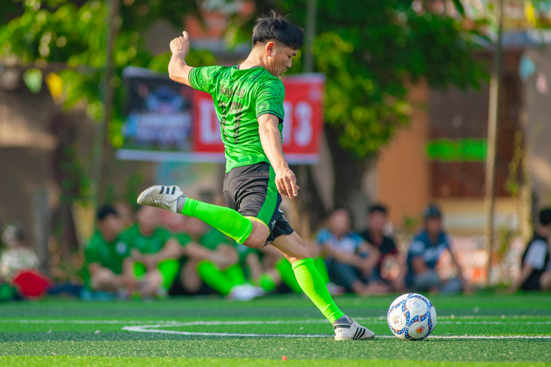 A soccer player in green uniform skillfully kicks the ball during a sports match in Hà Nội.