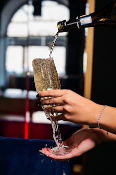 Close-up of a woman's hand elegantly pouring champagne into a tall flute glass indoors.