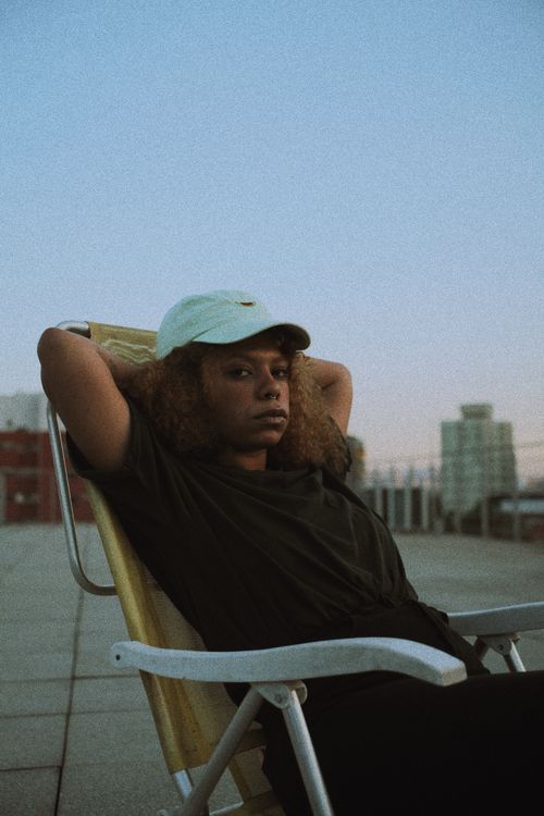 Free A woman in a cap sits on a chair, relaxing on a rooftop in São Paulo, Brazil. Stock Photo