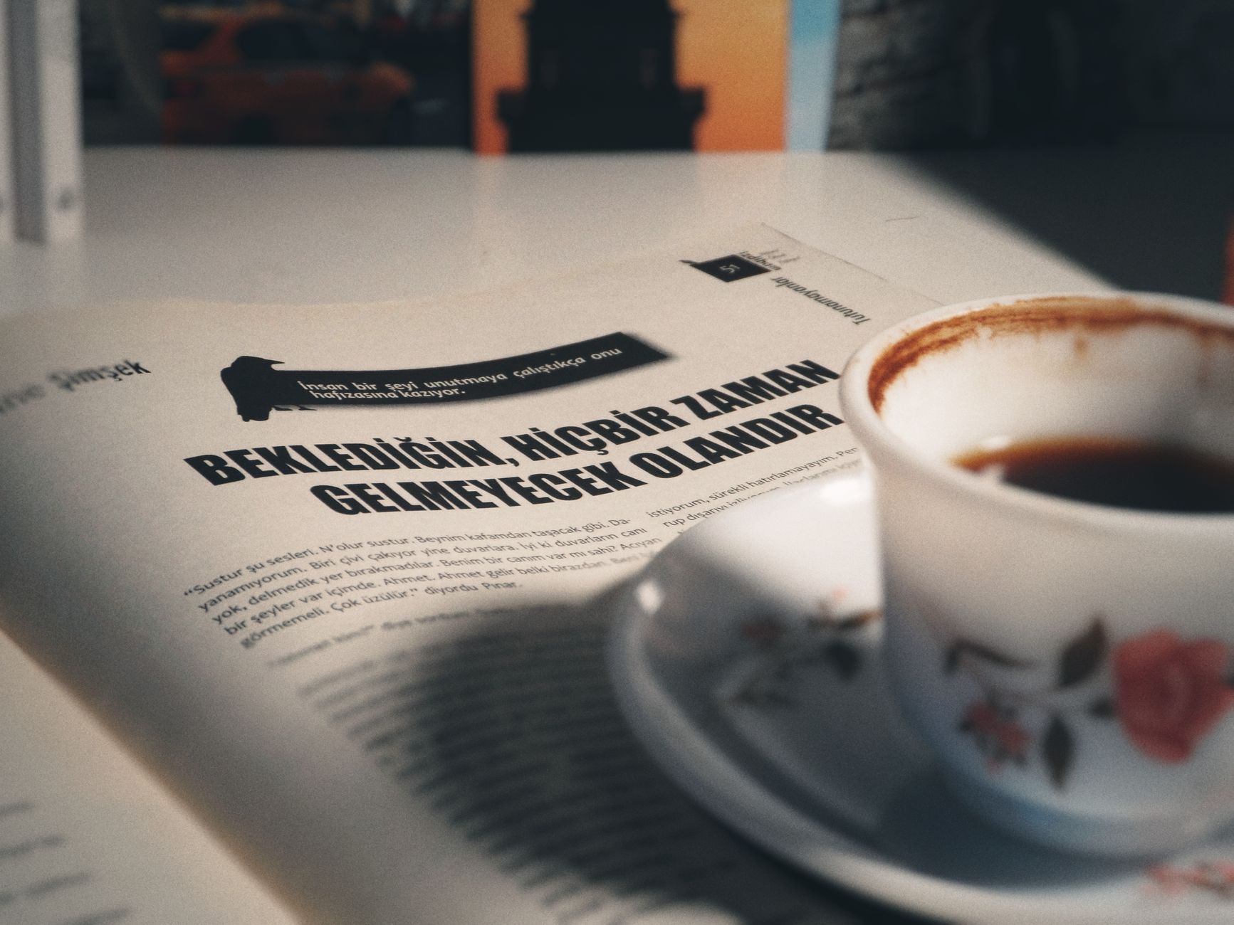 A porcelain coffee cup on a table with a Turkish magazine page in soft lighting.