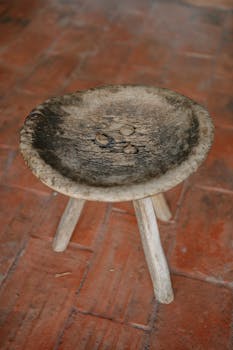 Antique rustic stool with a worn wooden seat showcasing vintage charm on a terracotta floor.