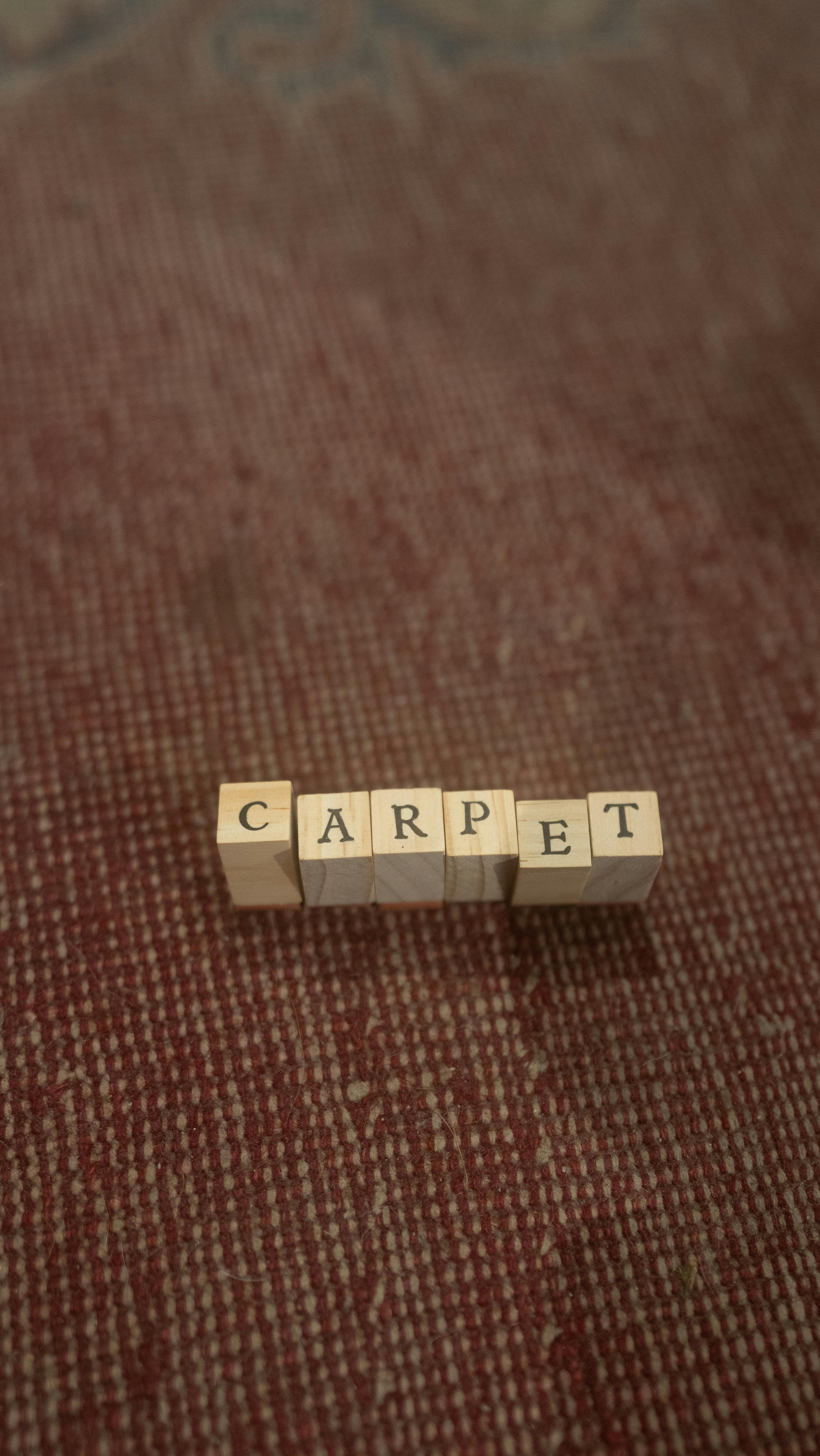 Gratis Treklosser som staver ordet "teppe" på en teksturert overflate. Arkivbilde