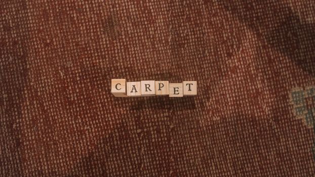 Wooden letter tiles spell 'carpet' on a textured rug surface. Simple and warm composition.