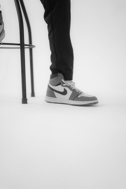 Free Close-up of a high-top sneaker worn by a person seated on a stool in a minimalist setting. Stock Photo