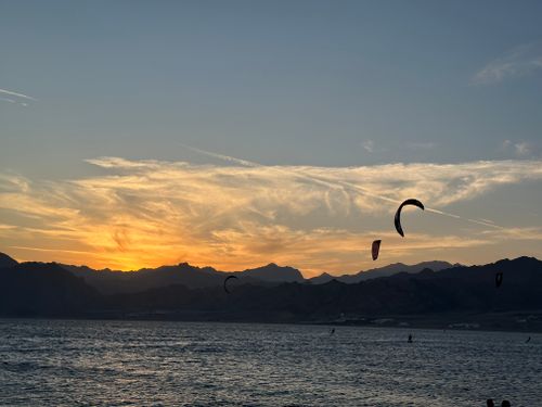 Free Silhouette of kitesurfers at sunset over a serene mountain backdrop and ocean waves. Stock Photo