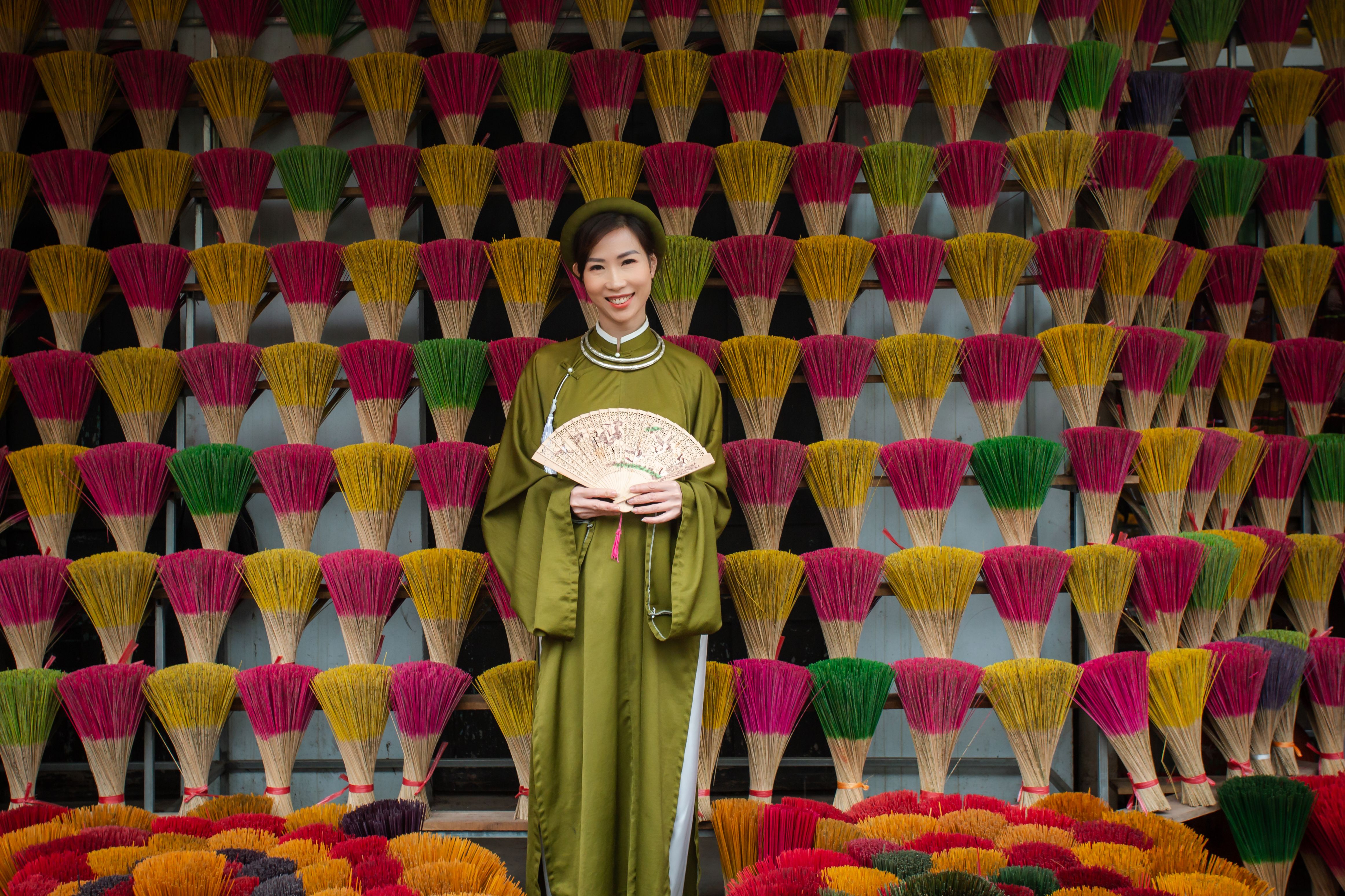 Portrait of a woman in traditional Vietnamese clothing surrounded by colorful incense sticks. Captured outdoors in Việt Nam.