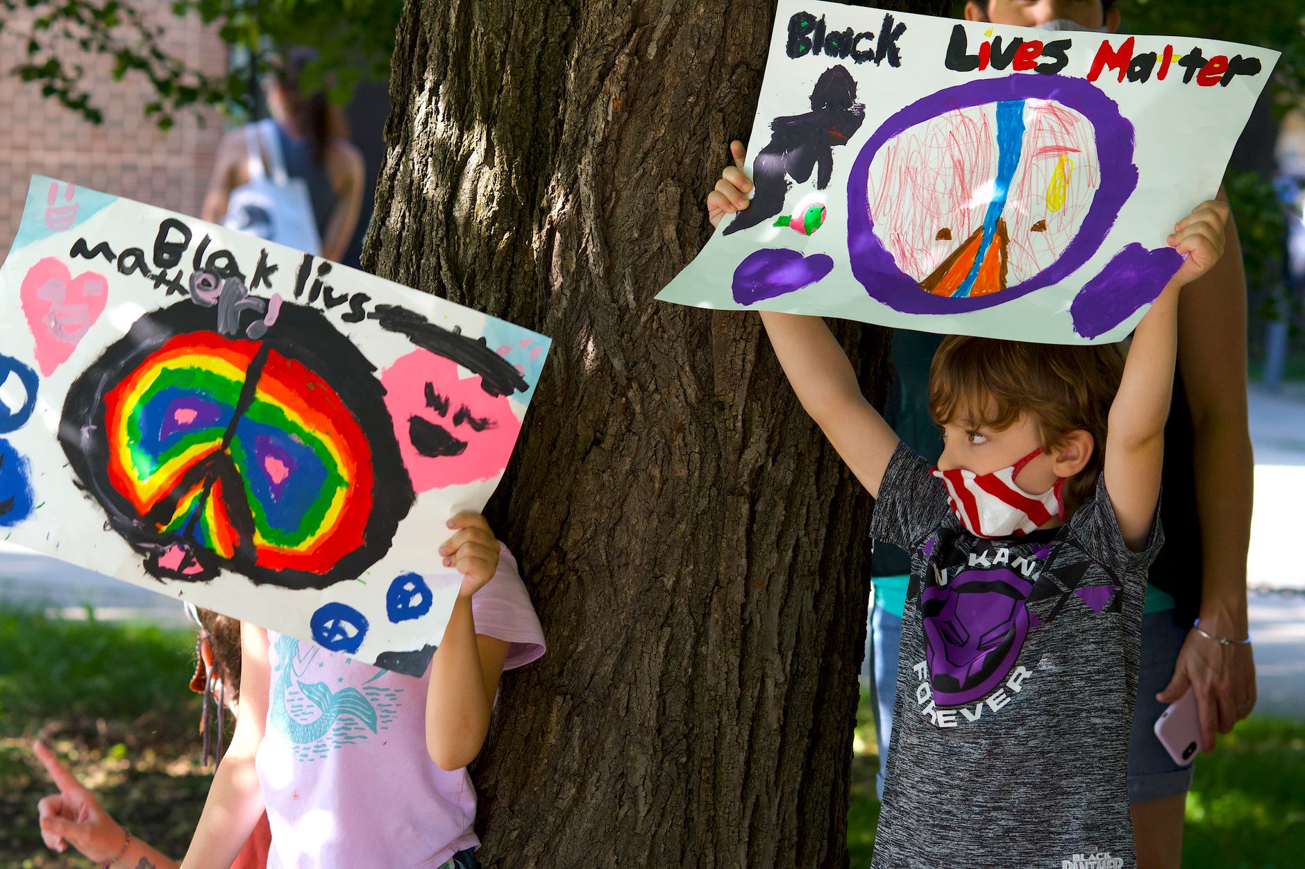 Children hold colorful Black Lives Matter signs in a peaceful outdoor protest.