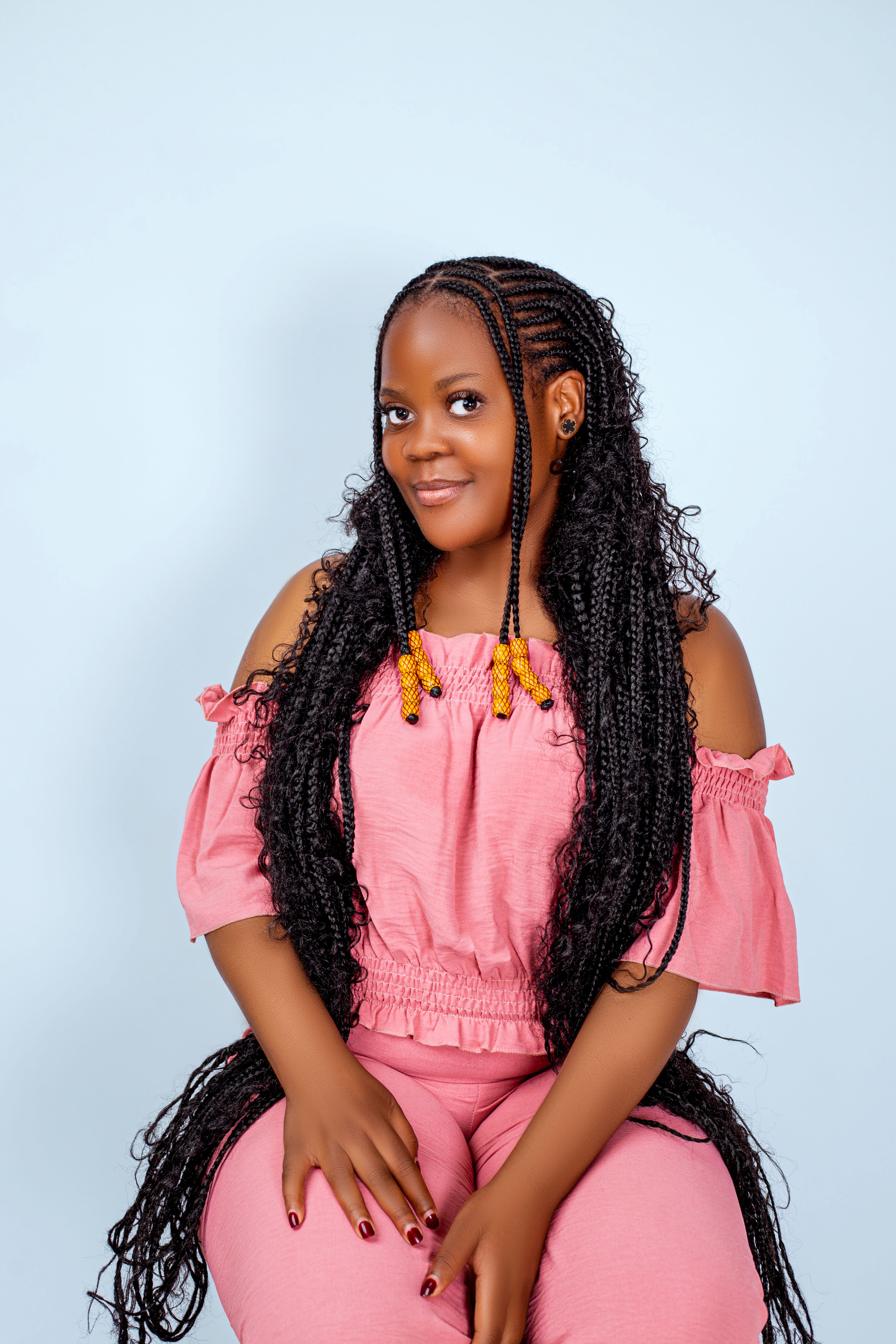 Portrait of a woman in pink attire with long braided hair on a soft background.