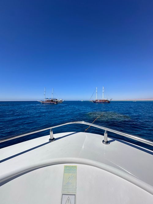 Free Peaceful scene of a boat on calm ocean, surrounded by clear blue sky and distant sailboats. Stock Photo