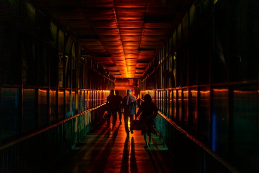 Silhouetted figures walking through a moody, illuminated urban tunnel at night.