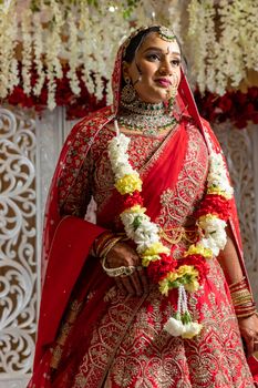 Beautiful Indian bride in red saree adorned with jewelry and floral garland, smiling.