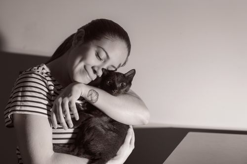 Free A woman lovingly hugs her black cat indoors, expressing warmth and affection. Stock Photo