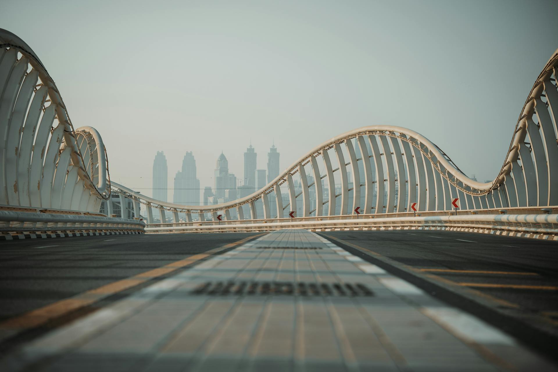 Curving bridge architecture leading towards a city skyline with skyscrapers, under a clear sky.