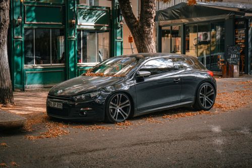 Free A sleek black car parked by a cafe on a leaf-strewn urban street in autumn. Stock Photo