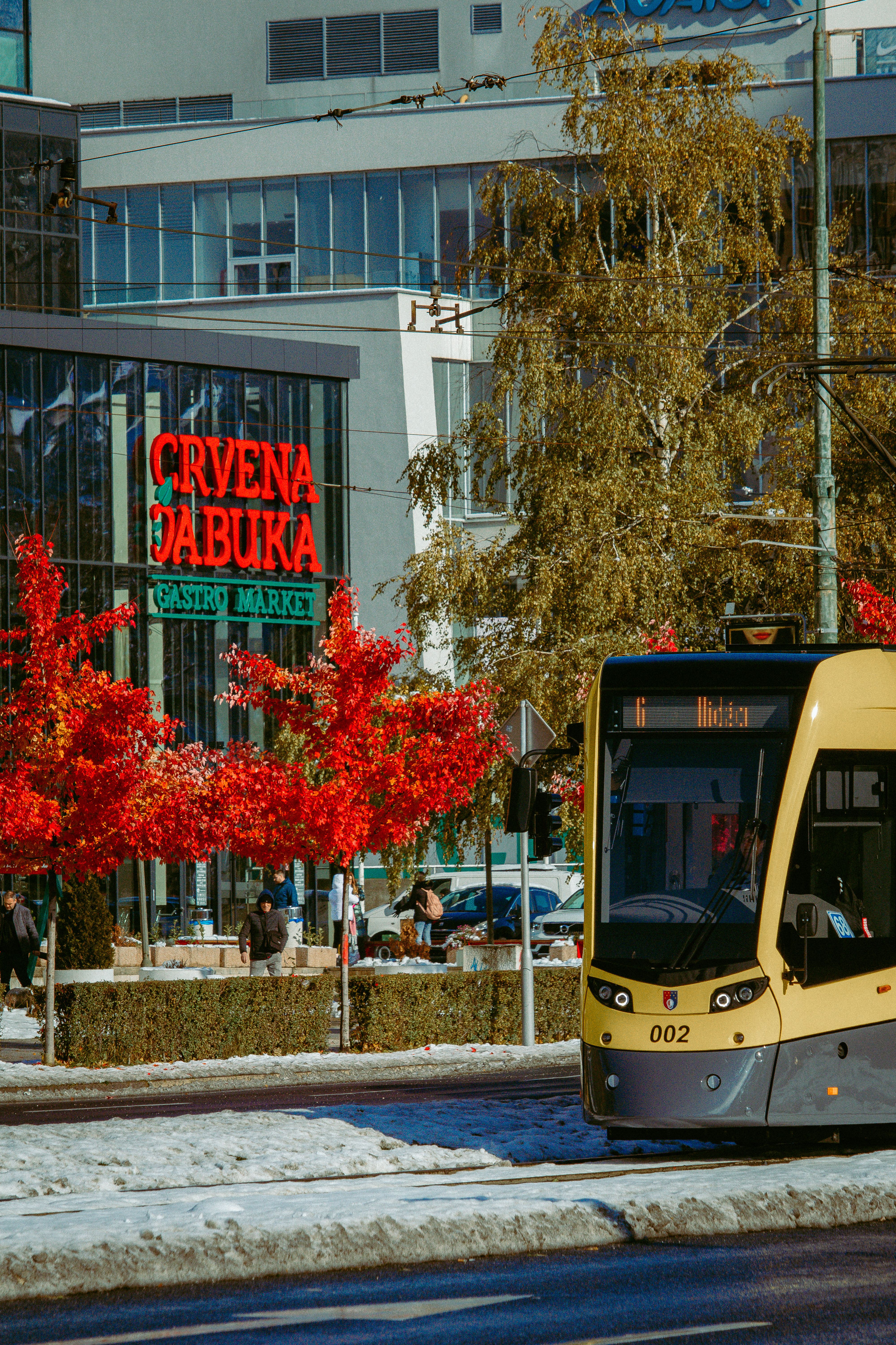 Colorful tram passes by a city street with vibrant autumn foliage and snow.