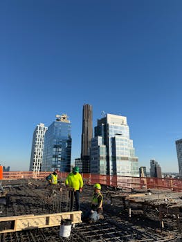 Aerial view of construction workers on a skyscraper site with city skyline in the background.