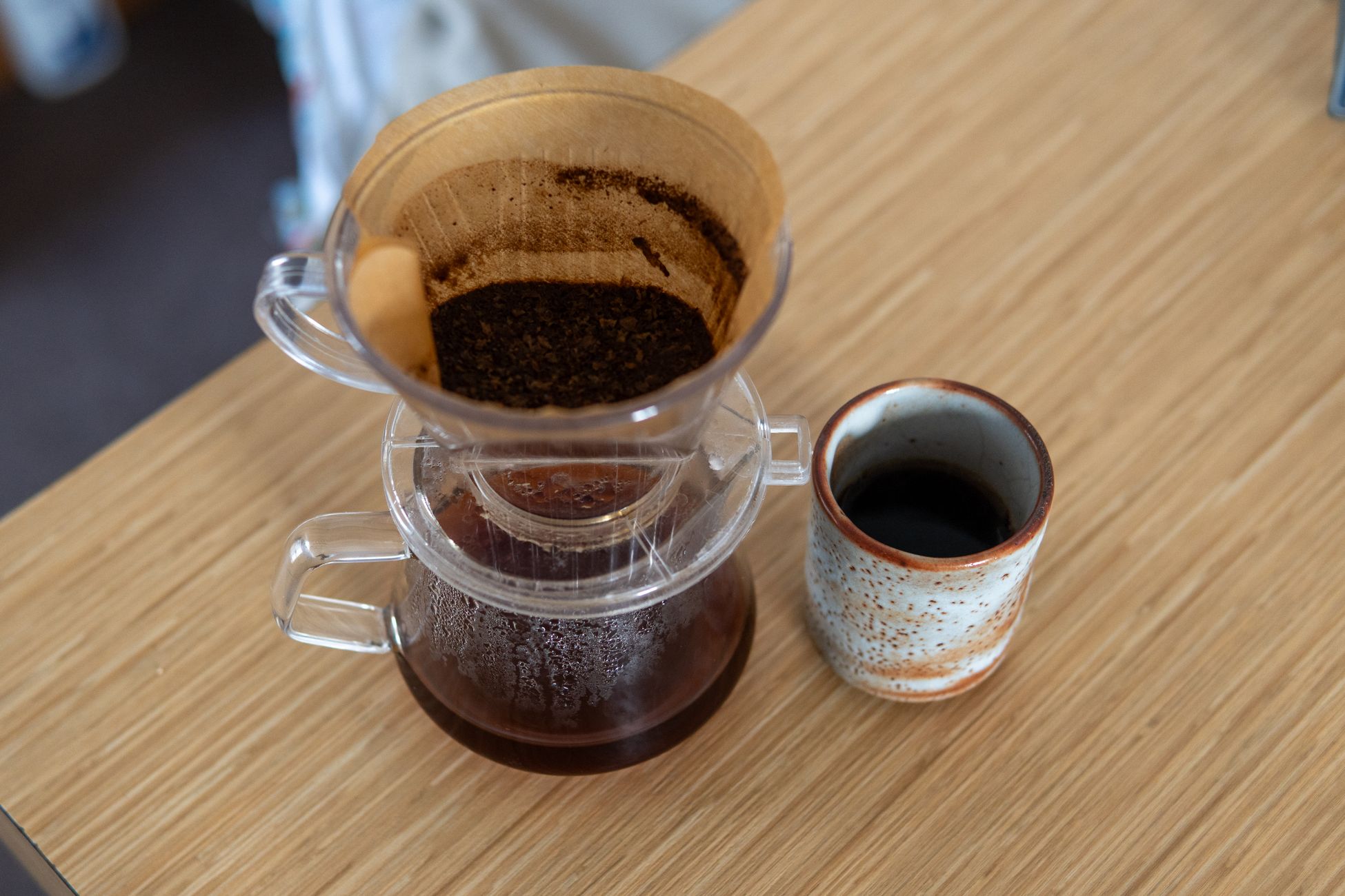 A cozy setup of drip coffee brewing with a paper filter and ceramic cup on a wooden table.