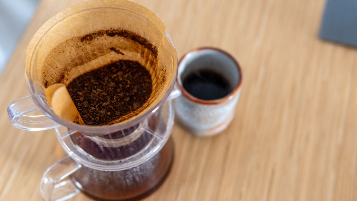 Pour-over coffee brewing into a ceramic mug on a wooden table