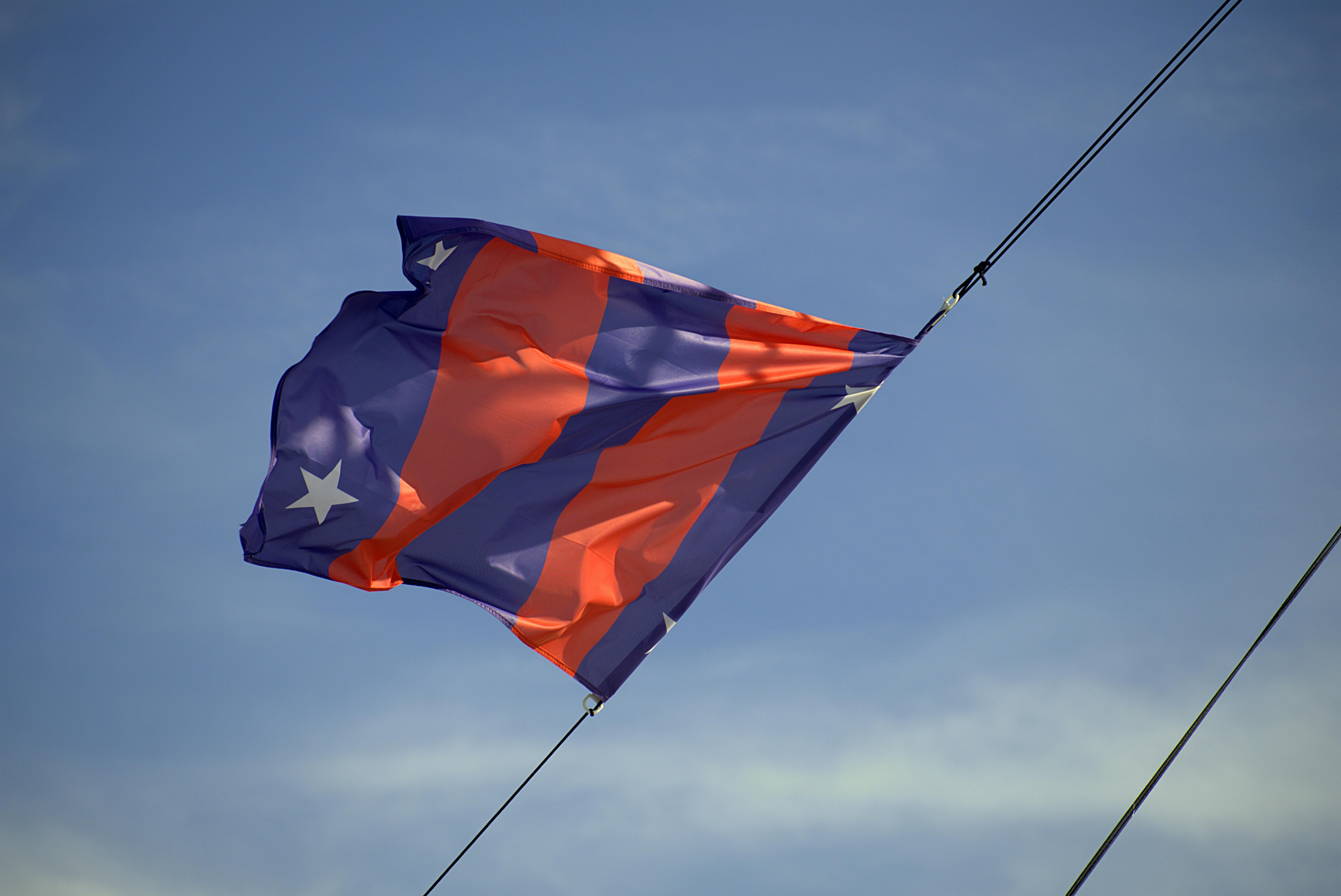 A vibrant orange and purple flag waves against a clear blue sky, symbolizing freedom.