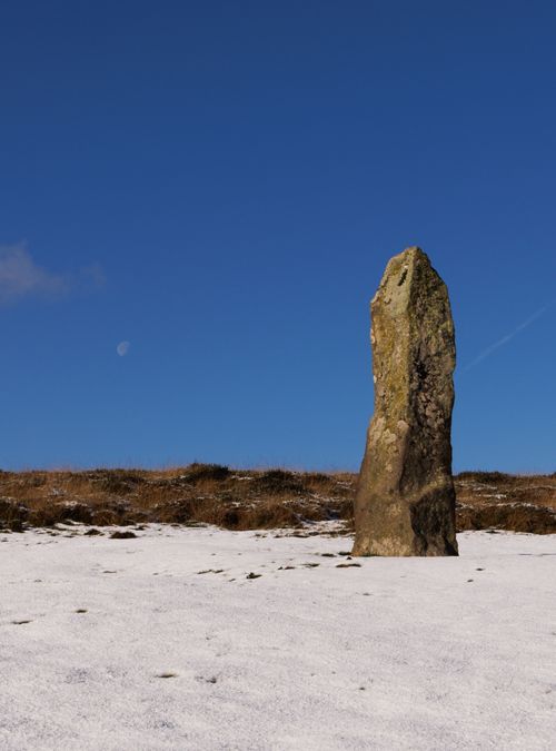 Free Monolithic stone standing upright on a snowy field under a clear blue sky. Stock Photo