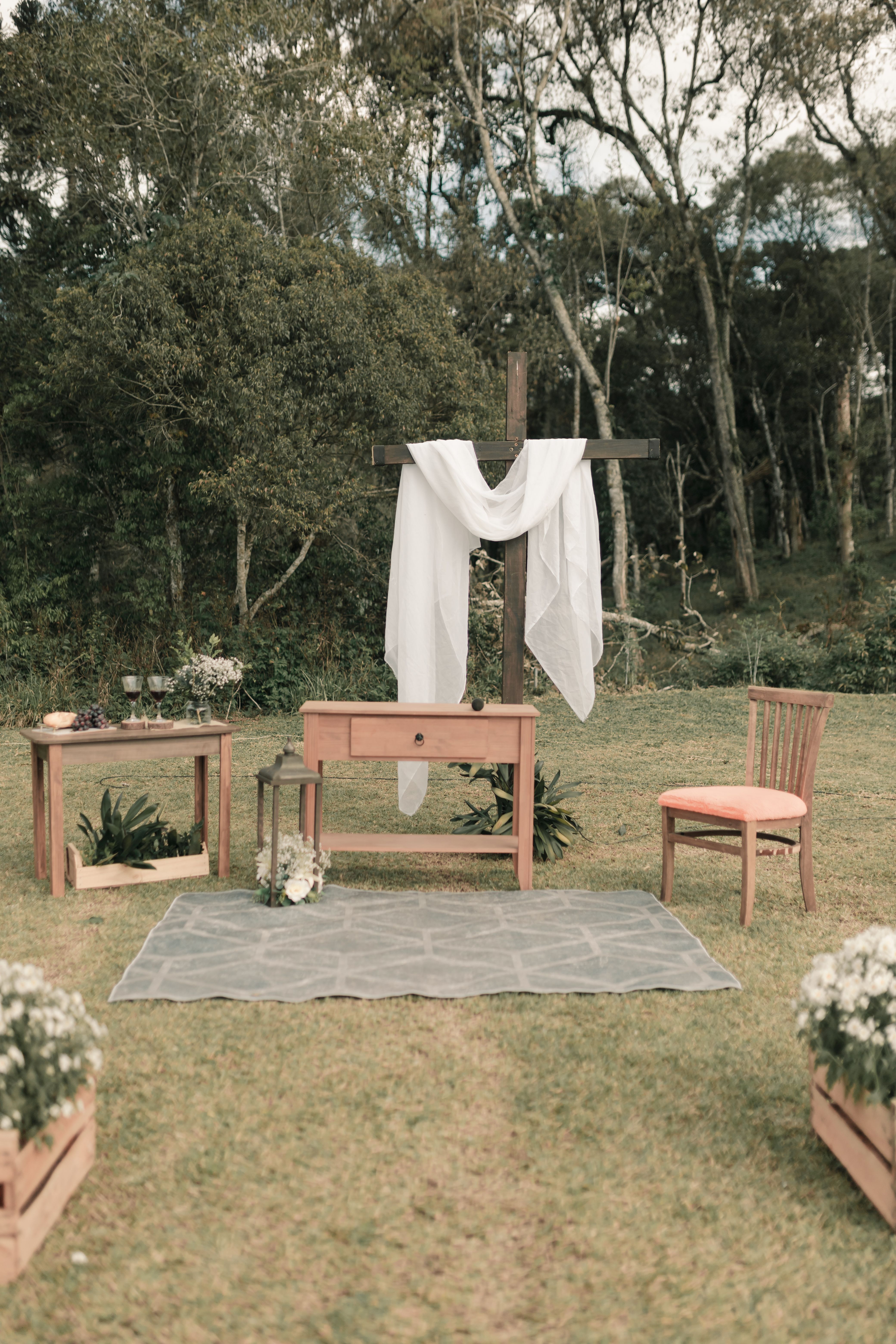 Fotomural Un altar rústico de boda al aire libre con cruz, mesa y silla en la naturaleza.