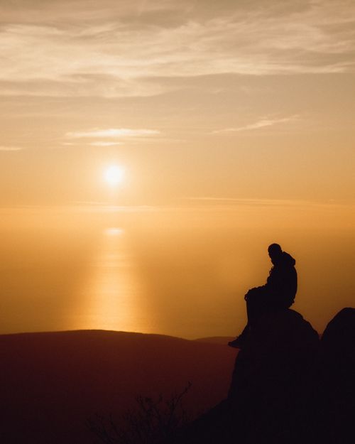Free Silhouette of a person sitting on rocks observing a stunning ocean sunset. Stock Photo