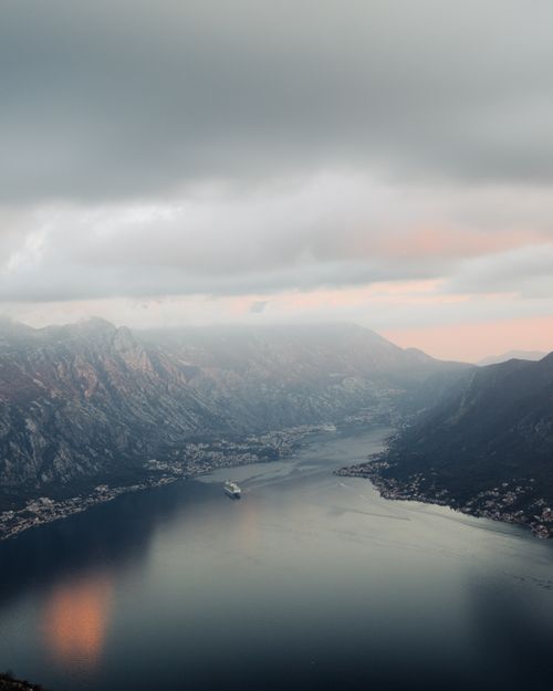 Free A stunning view of a bay surrounded by mountains at sunset, with a cruise ship sailing. Stock Photo