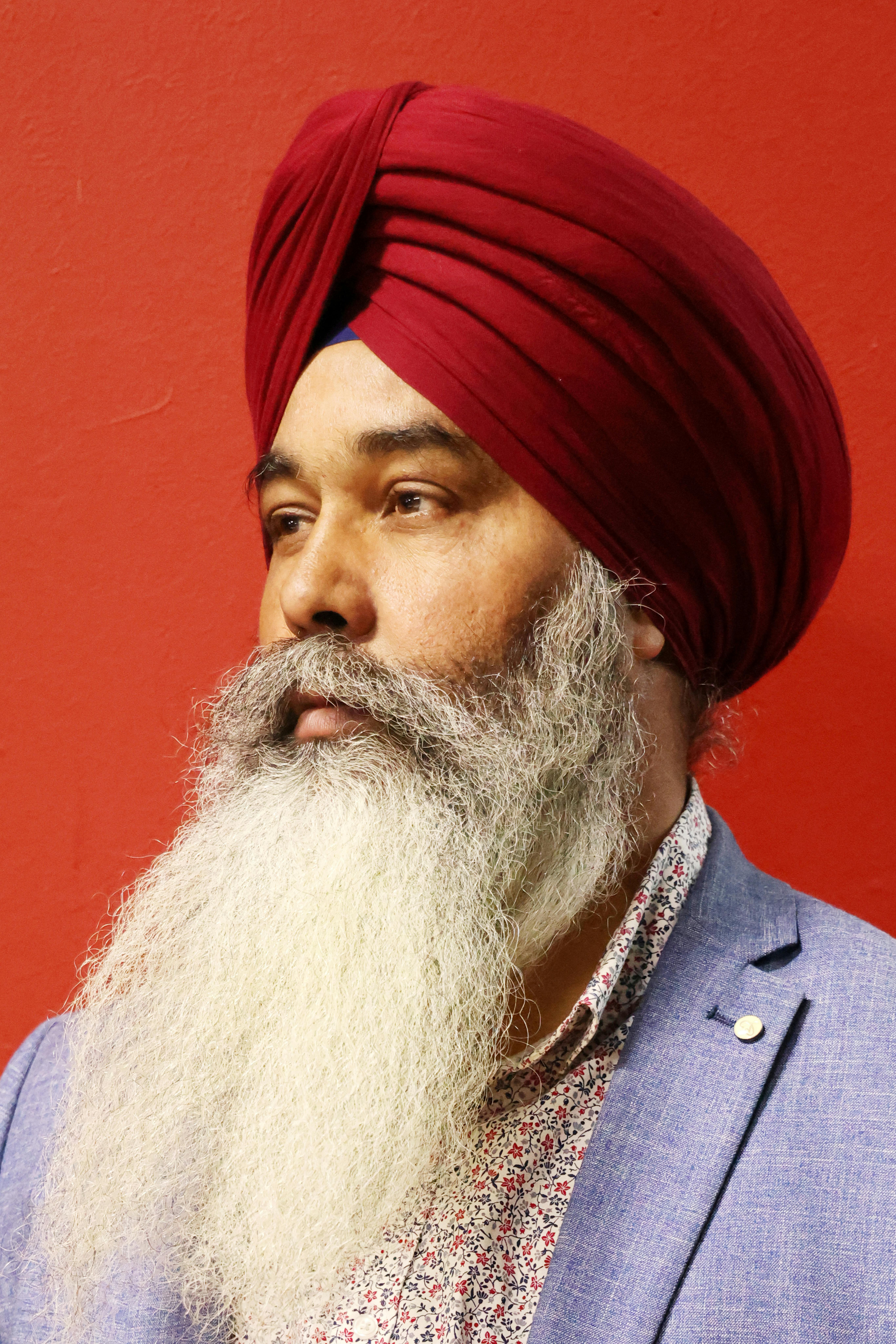 Elegant portrait of a man with a red turban and grey beard against a bold red background.