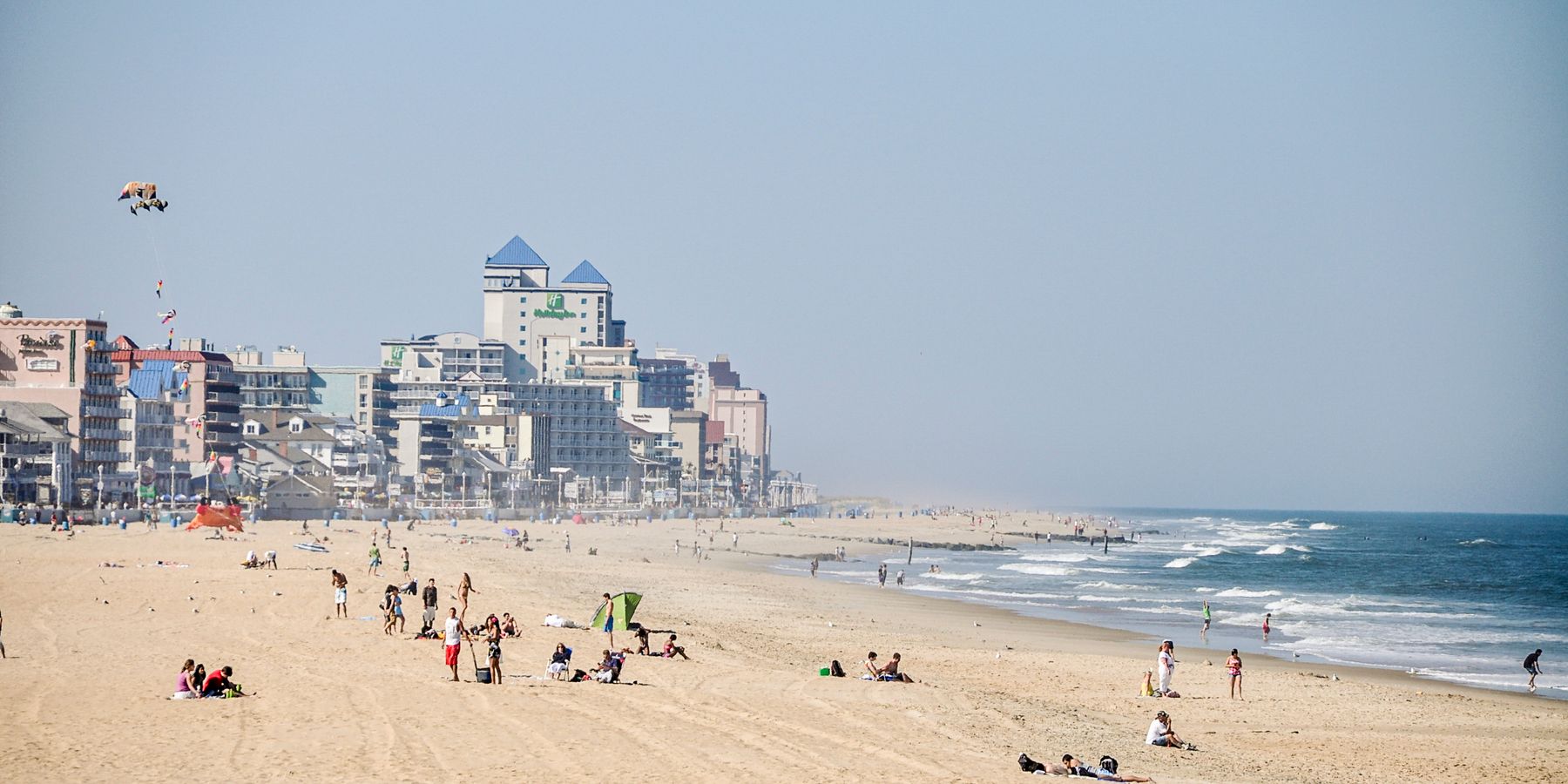 People enjoying a sunny day at a busy beach near waterfront hotels and buildings.