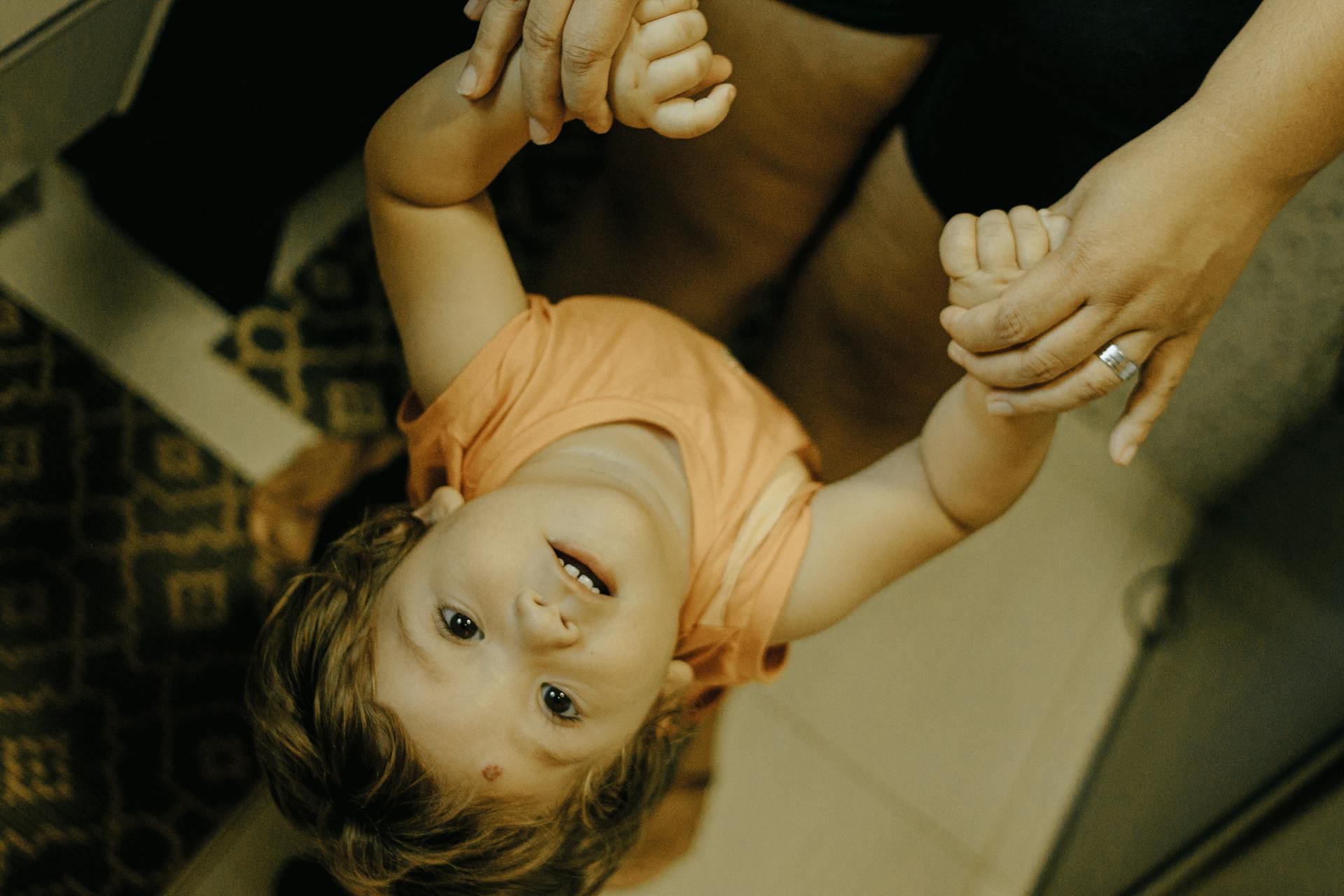 A happy child holds hands with a parent indoors, expressing excitement and connection.