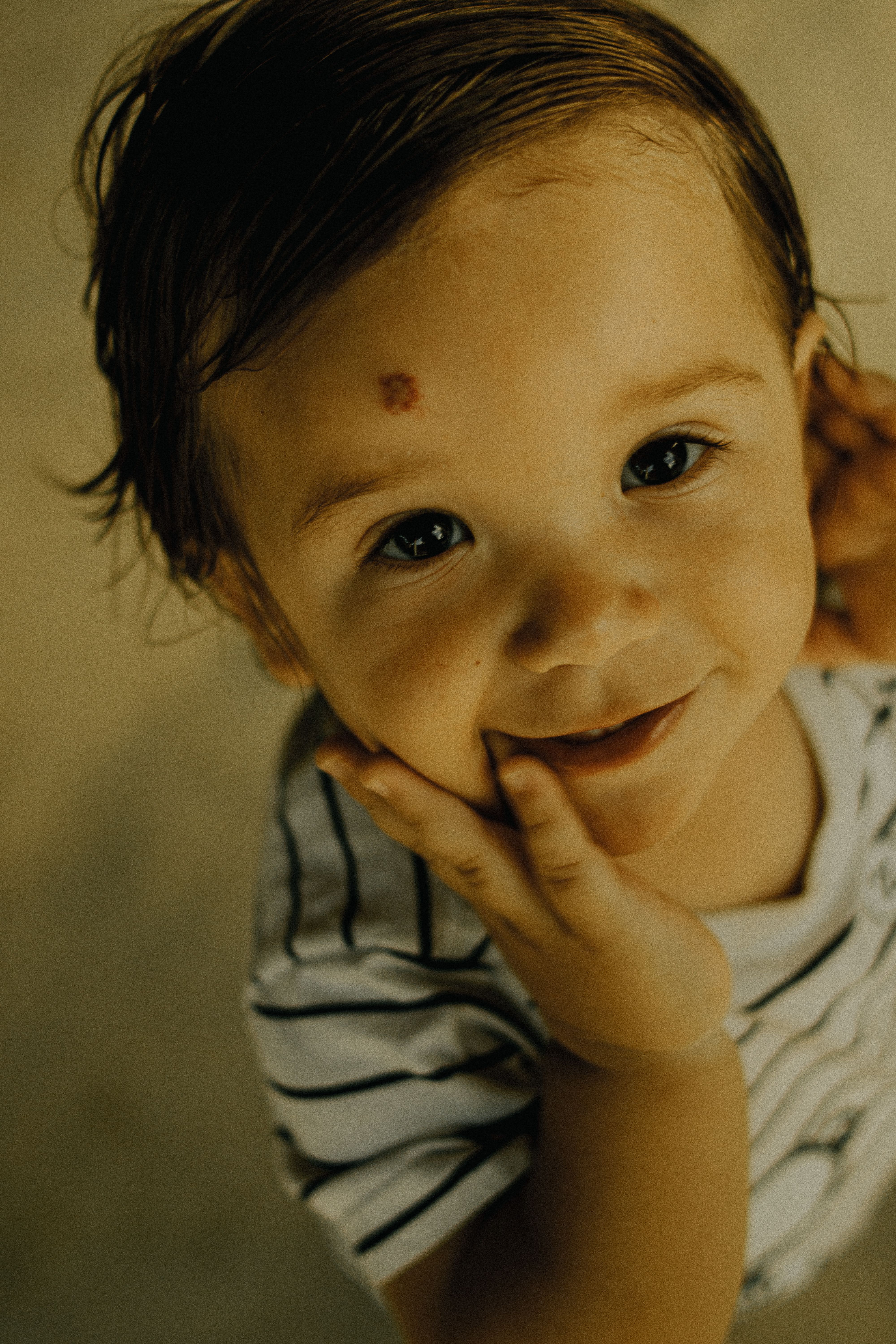 Adorable toddler smiling brightly, looking up with curiosity in a casual setting.