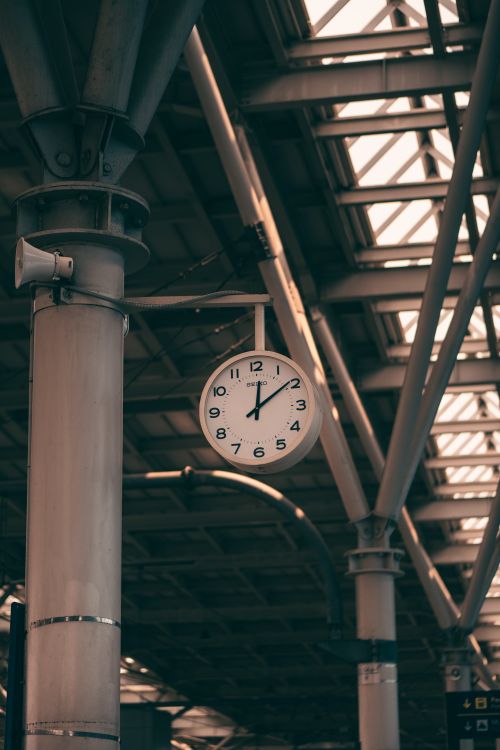 Free A vintage-style clock hanging in an industrial train station interior, showcasing architectural details. Stock Photo