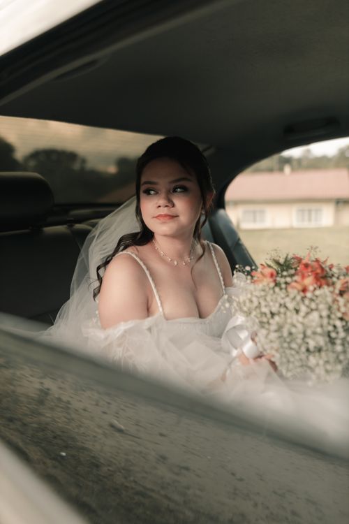 Free Beautiful bride in a wedding gown holding a bouquet while seated in a car. Stock Photo