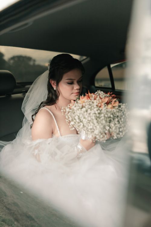 Free Bride sits in a vintage car holding a floral bouquet, exuding elegance and romance. Stock Photo