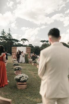 Beautiful outdoor wedding ceremony with guests and flower decor under cloudy sky.