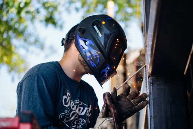 Skilled worker producing sparks while welding outdoors