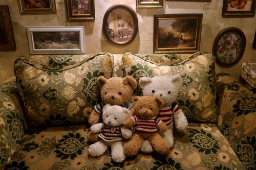 Free A cozy vintage room with teddy bears on a patterned sofa surrounded by framed art. Stock Photo