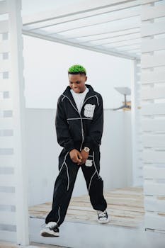 Young adult with green hair in modern tracksuit posing in bright outdoor setting.