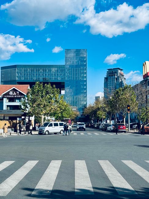 Sunny day at a bustling street crossing in Tianjin, showcasing modern architecture and vibrant city life.