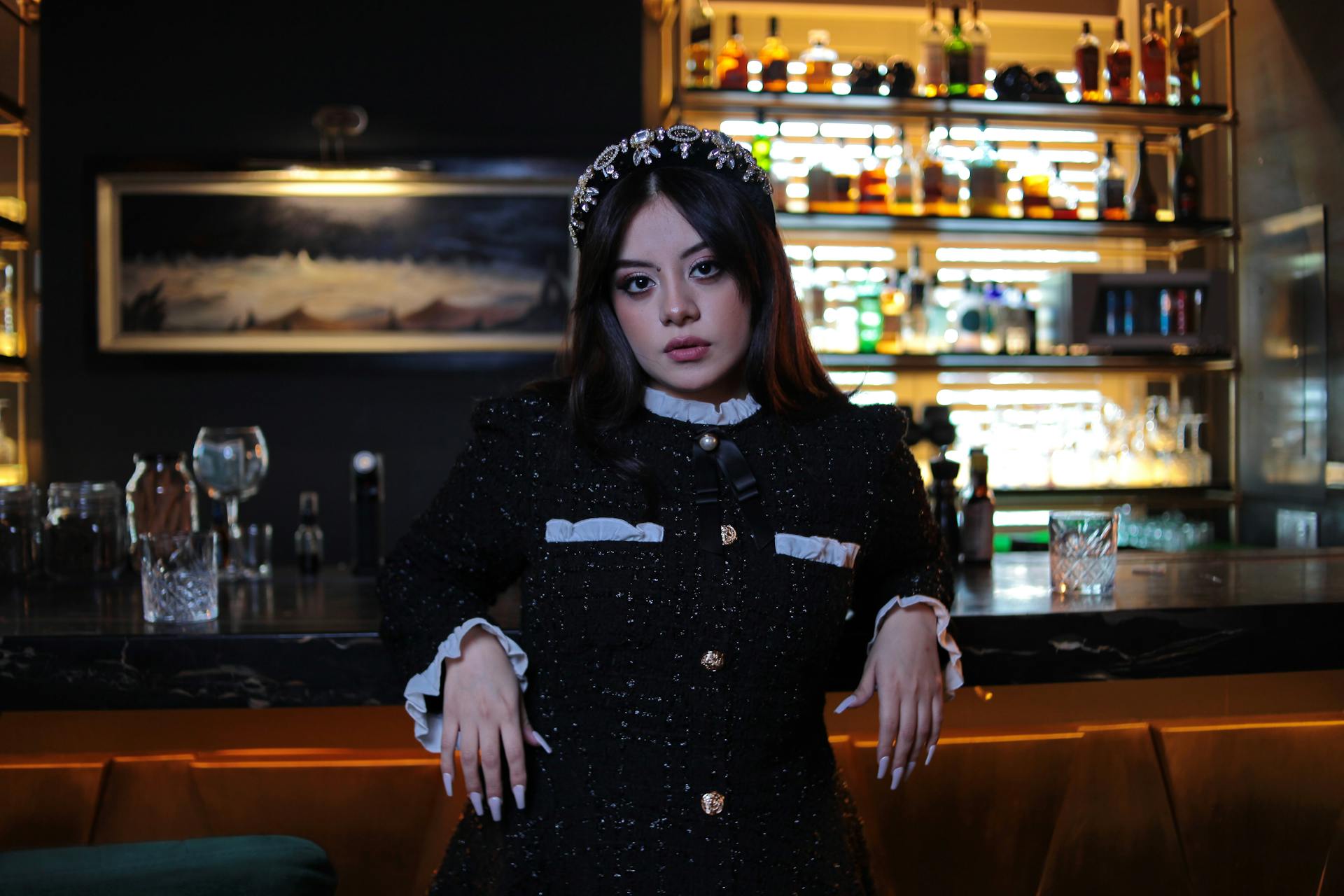 A fashionable woman in a chic outfit posing confidently in an upscale cocktail bar.